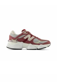Zapatilla roja y beis con materiales de malla y ante, que cuenta con una suela intermedia blanca y gruesa, un prominente logo "N" y detalles texturizados en el talón.