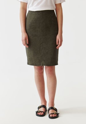 Jupe-crayon en lin vert olive avec une finition texturée, mi-longue, présentant une coupe slim et un design simple. Portée avec des sandales noires.