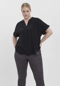 Zwarte blouse met korte mouwen en een V-hals, met een zachte textuur en een ontspannen pasvorm, gecombineerd met donkergrijze aansluitende pants met ritsaccenten.