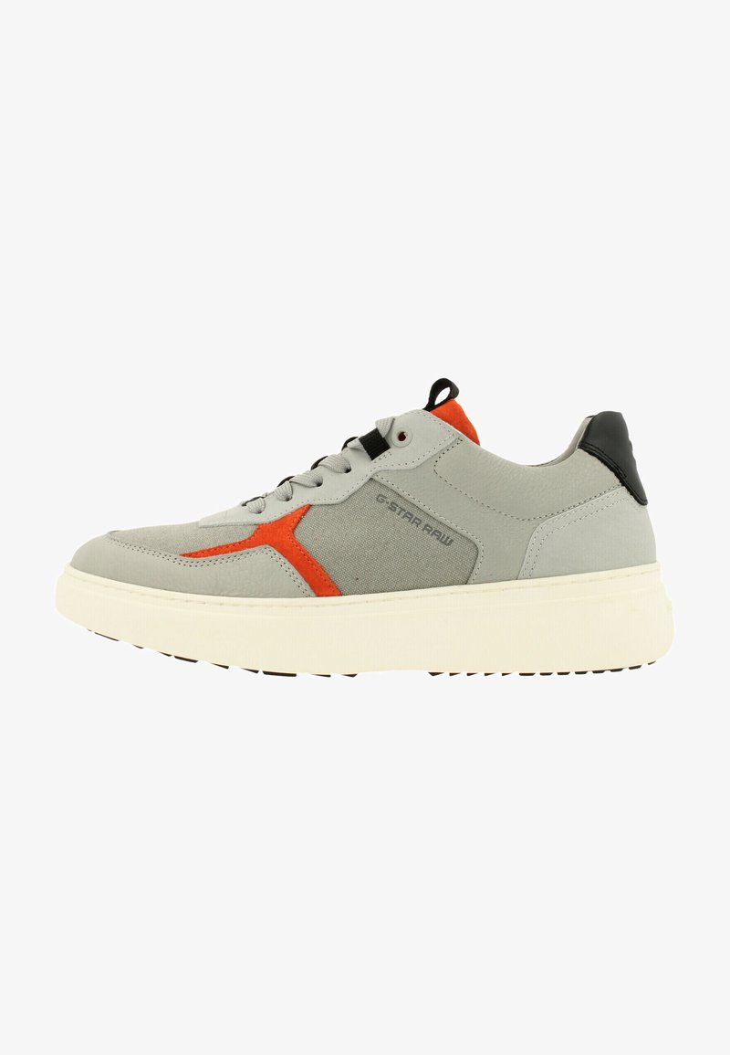 Grijze sport schoen met een oranje accent en een zwarte hiel. Kenmerkt zich door een gestructureerde bovenkant en een dikke witte zool met een gemusterde onderkant.