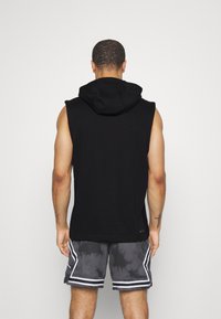 Felpa nera senza maniche con cappuccio, abbinata a pantaloni corti grigi con un motivo tie-dye e accenti bianchi. Abbigliamento sportivo casual.