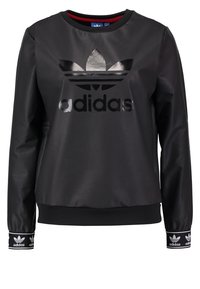 Czarna bluza z połyskującym wykończeniem, z dużym czarnym logo Adidas. Mankiety ściągane ściągaczem z dodatkami logo, okrągły dekolt i luźny krój.