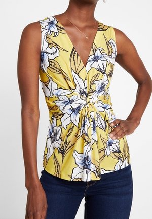 Żółty top bez rękawów z głębokim dekoltem w kształcie litery V, zdobiony kwiatowym wzorem w odcieniach niebieskiego i białego. Marszczony węzeł w talii; gładka tkanina.