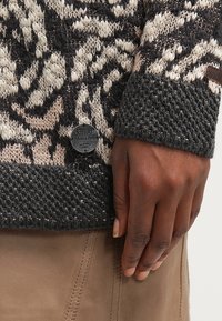 Sweter Khujo o dzianinowej fakturze, z czarno-beżowym wzorem, ściągaczami na rękawach i okrągłą naszywką z logo.