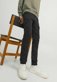 Pantalon cargo noir avec poches latérales, coupe fuselée et poignets élastiques, porté avec des baskets blanches, associé à un sweatshirt gris.