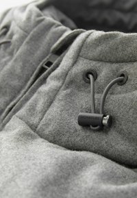 Tela gris con un acabado texturizado. Presenta un cordón ajustable con un cierre de cordón negro etiquetado como "SIGNATURE". Diseño simple, sin patrones.