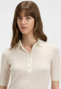 Top polo in maglia color avorio, con maniche corte, texture a coste, colletto e patta con cinque bottoni.