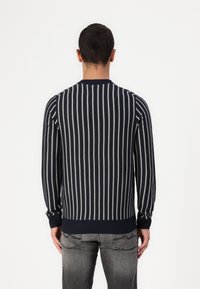 Navy gestreifter Strickpullover mit weißen vertikalen Streifen, geripptem Ausschnitt und Bündchen, slim fit, über grauen Jeans getragen. Rückansicht.