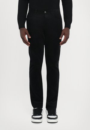 Sorte corduroy bukser med slim fit, fem-lomme design og metalknaplukning. Båret med sorte og hvide sneakers.