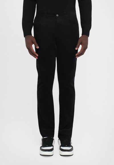 Μαύρο παντελόνι κοτλέ σε slim fit, σχεδίαση με πέντε τσέπες και κλείσιμο με μεταλλικό κουμπί. Φοριέται με μαύρα και άσπρα αθλητικά παπούτσια.