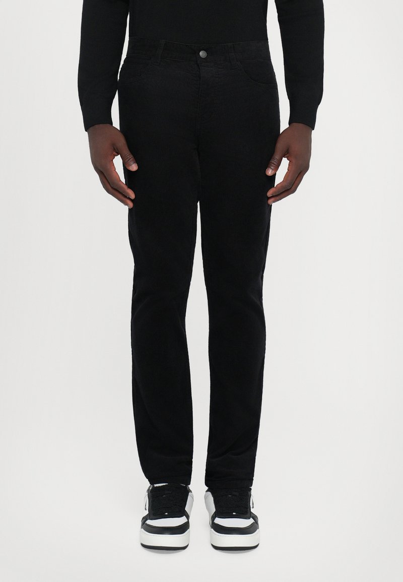 Sorte corduroy bukser med slim fit, fem-lomme design og metalknaplukning. Båret med sorte og hvide sneakers.
