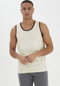 Lys gul tanktop med marineblå kant, prydet med et hvidt grafisk tryk "Original Raw Denim Co." i midten. Blødt stof, afslappet pasform.
