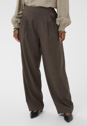 Platus kelnes iš tamsiai rudos medžiagos su vertikaliomis raukšlėmis. Medžiaga turi subtilią tekstūrą. Su jomis derinami juodi bato forma įsmailėti bateliai.