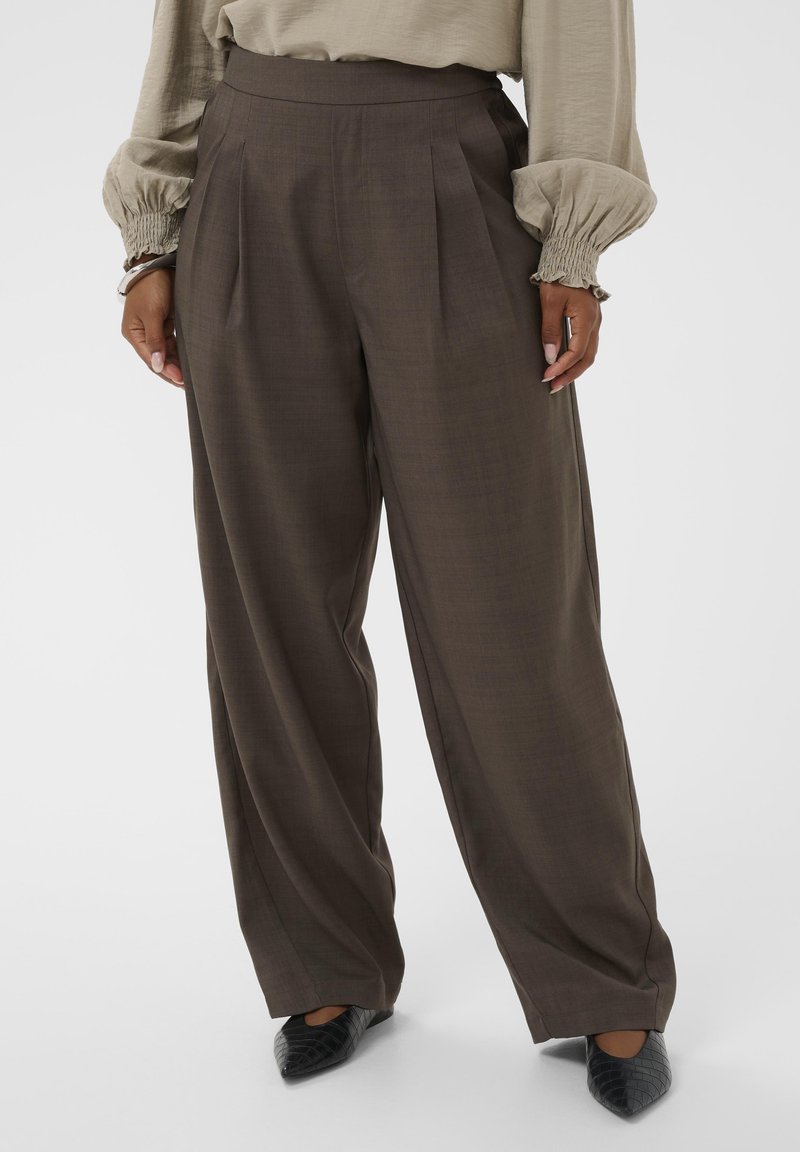 Laia püksid tumepruunist kangast, vertikaalsete voldikute ja peene tekstuuriga. Sobitatud mustade terava ninaga kingadega.