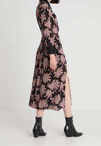 Svart långärmad klänning med blommigt rosa mönster, sidöppning och svart krage. Matchas med glänsande svarta ankelstövlar.