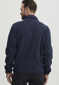 Marineblaue Fleecejacke mit hohem Kragen, ausgestattet mit einer strukturierten Oberfläche und einem kleinen Rückenpasse-Detail. Elastische Bündchen und Saum sorgen für einen angenehmen Sitz.