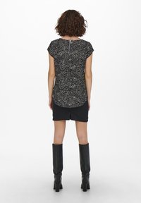 Haut noir à motifs avec manches courtes, encolure ronde et fermeture éclair au dos ; assorti à une jupe en denim noir et des bottes noires montantes jusqu'au genou.