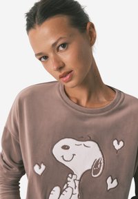 Brun fleece-sweatshirt med en hvid tegneseriehund med et glad udtryk og hjerteformer. Rund halsudskæring og afslappet pasform.