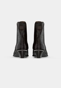 Botas de tornozelo pretas com um acabamento em croco texturizado, com saltos afunilados e pequenas alças na parte de trás. Forro interior suave.