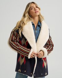 Ullblandings oversized jakke med marineblå bunn, kremfarget fuskepelskrage, fargerike tribal-mønstrede ermer og dekorative låsebeslag.