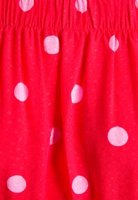 Tecido vermelho com bolinhas brancas. A textura parece suave e ligeiramente texturada, com um detalhe de cintura elástica.