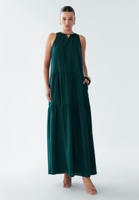 Robe maxi verte sans manches avec un design à volants, un col rond avec une ouverture en forme de clé et des poches latérales. Tissu doux et fluide.