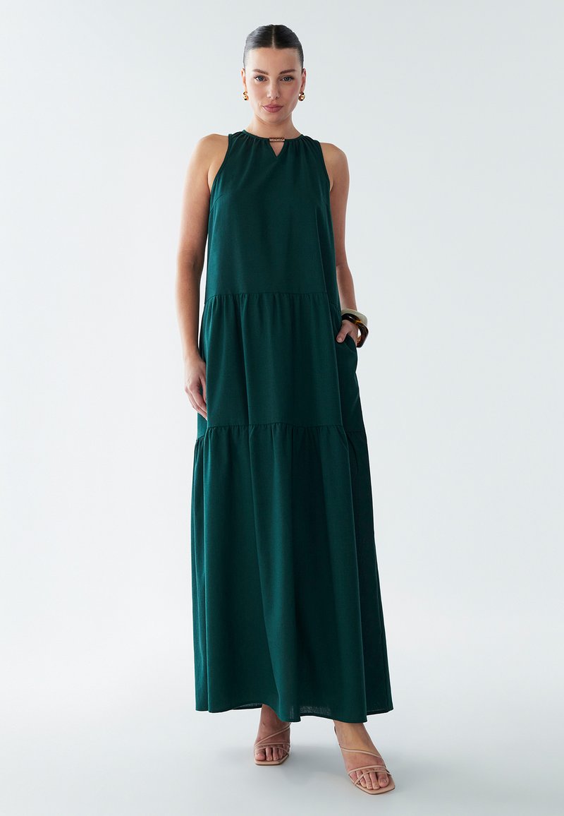 Žalia maksi suknelė be rankovių, su raktu kaklo iškirpte, sluoksniuota sijonu ir kišenėmis. Pagaminta iš minkštos, lengvai krentančios medžiagos.