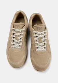 Beige suede sneakers with white perforated laces. Rounded toe design and subtle stitching details on the upper. Rubber sole with light texture.