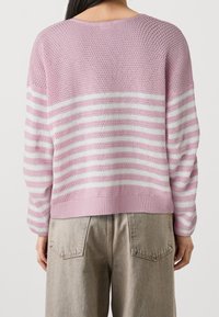 Pull en tricot rose avec des rayures horizontales blanches, offrant une coupe décontractée, un col rond, et un ourlet et des poignets côtelés. Design en maille ouverte texturée.