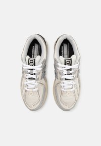 Baskets en mesh blanches avec des accents gris, présentant une tige texturée, une semelle rembourrée et des lacets blancs. Marque "New Balance" visible sur la languette.