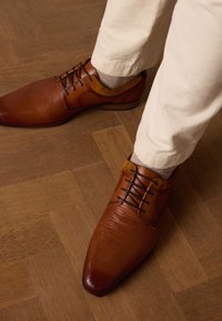 Bruine leren schoenen met een gestructureerde afwerking, spitse neuzen, donkere veters en een contrasterende tan suède accent bij de enkel, gecombineerd met lichte broeken.