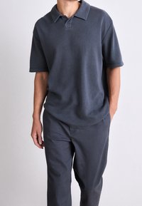 Tummanharmaa, lyhythihainen polo-paita, jossa on ribbatun tekstuurin ja klassinen kaulus, yhdistettynä samansävyisiin harmaisiin housuihin. Rentoa leikkausta.