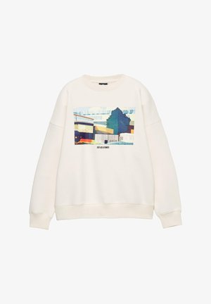 Sweat-shirt couleur crème à manches longues avec un col arrondi. Présente une impression graphique colorée de bâtiments et d'un arbre sur le devant.