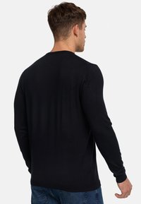 Chemise noire à manches longues avec un col rond. Présente un design lisse et ajusté avec des poignets côtelés. Tissu uni, sans motifs ni accents visibles.