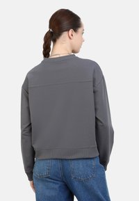 Sudadera gris con un corte relajado, puños y dobladillo acanalados. Textura suave con una costura horizontal en la parte posterior, combinada con jeans azules.