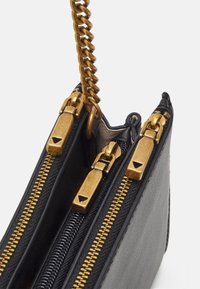 Černá a šedá strukturovaná kabelka se zlatým řetízkovým popruhem. Má tři oddělené přihrádky na zip se zlatým kováním a texturovanými materiály.