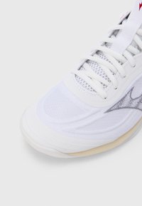 Λευκό αθλητικό παπούτ�σι με πάνελ από δίχτυ, υφή σχεδίου και μπεζ ελαστική σόλα με διακριτικές λεπτομέρειες.