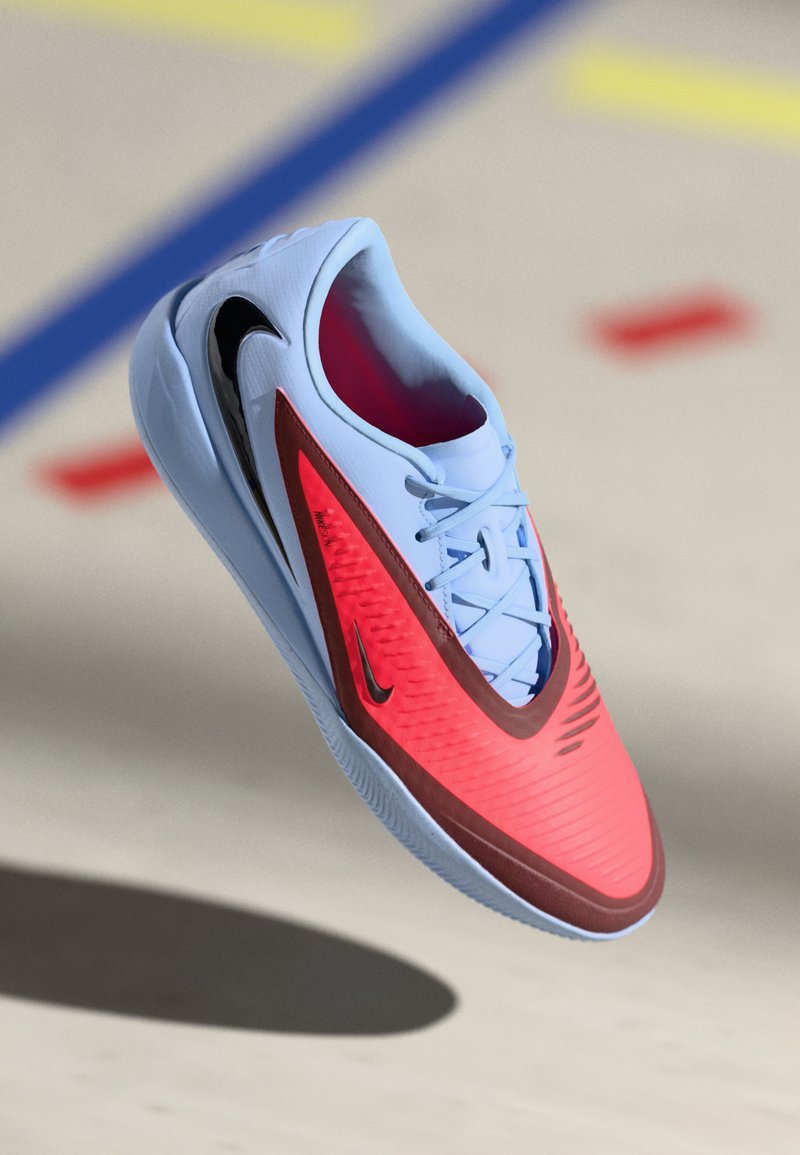 Nike athletic shoe featuring a light blue upper, a bright red side panel, textured design, and a black swoosh logo.