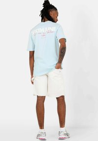 Ljusblå t-shirt i bomull med korta ärmar, prydd med vit text på baksidan. Matchas med vita denimshorts och silverskor för löpning.