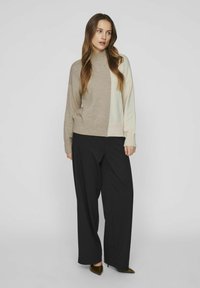 Beige en lichtgroen blokkleurig trui met een hoge halslijn, geribbelde zoom en lange mouwen, gecombineerd met brede zwarte broek.