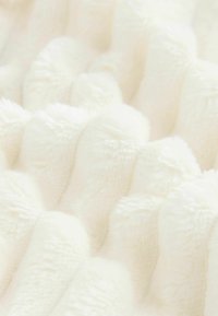 White plush blanket with a wavy, textured surface. Features soft, fluffy fibers arranged in a rippled pattern, creating a cozy appearance.