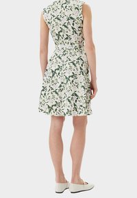 Blumendruckkleid mit grünen Blättern und lila Akzenten. Ärmelloses Design, tailliert und mit ausgestellt Rock. Glattes Material, knielang.