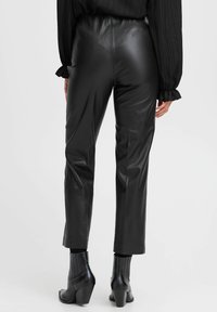 Pantaloni in ecopelle neri, a vita alta e slim fit, con una texture liscia e una lunghezza cropped. Indossati con stivali neri alla caviglia.