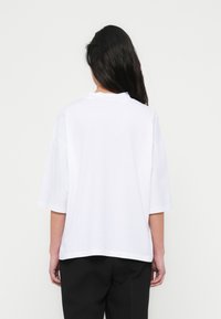 Άσπ ρο φαρδύ μπλουζάκι με κοντά μανίκια, στρογγυλεμένο λαιμόκοψη και άνετη εφαρμογή. Μαλακό βαμβακερό ύφασμα με λεία υφή.