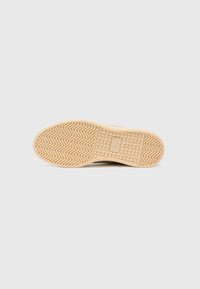 Semelle d'une sneaker avec un motif texturé et ondulé en beige. La base est plate, avec un accent rectangulaire près du centre.