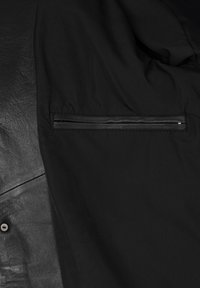 Chaqueta negra que presenta un material de cuero en un lado y un tejido suave en el otro, con un detalle de bolsillo con cremallera.