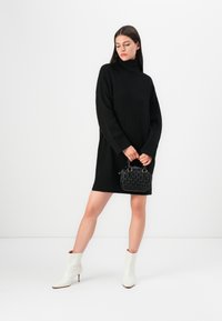 Must mustreh dress kõrge kaelusega, millele on lisatud väikene tekstuuriga must käekott ja valged säärekingad terava ninaga.