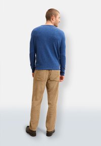 Blauer Langarmpullover mit strukturiertem Finish, kombiniert mit beigen Cordhosen, die über Gesäßtaschen verfügen, und braunen Schuhen.