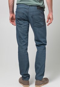 Sinisistä farkuista kapealahkeiset, joissa kaksi takataskua ja pieni logotunniste. Kangas on sileä ja hieman kiiltävä.