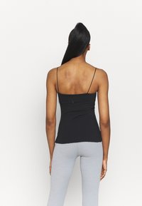 Black spaghetti strap top with a scalloped hem, fitted design, and smooth texture, paired with light gray fitted pants.